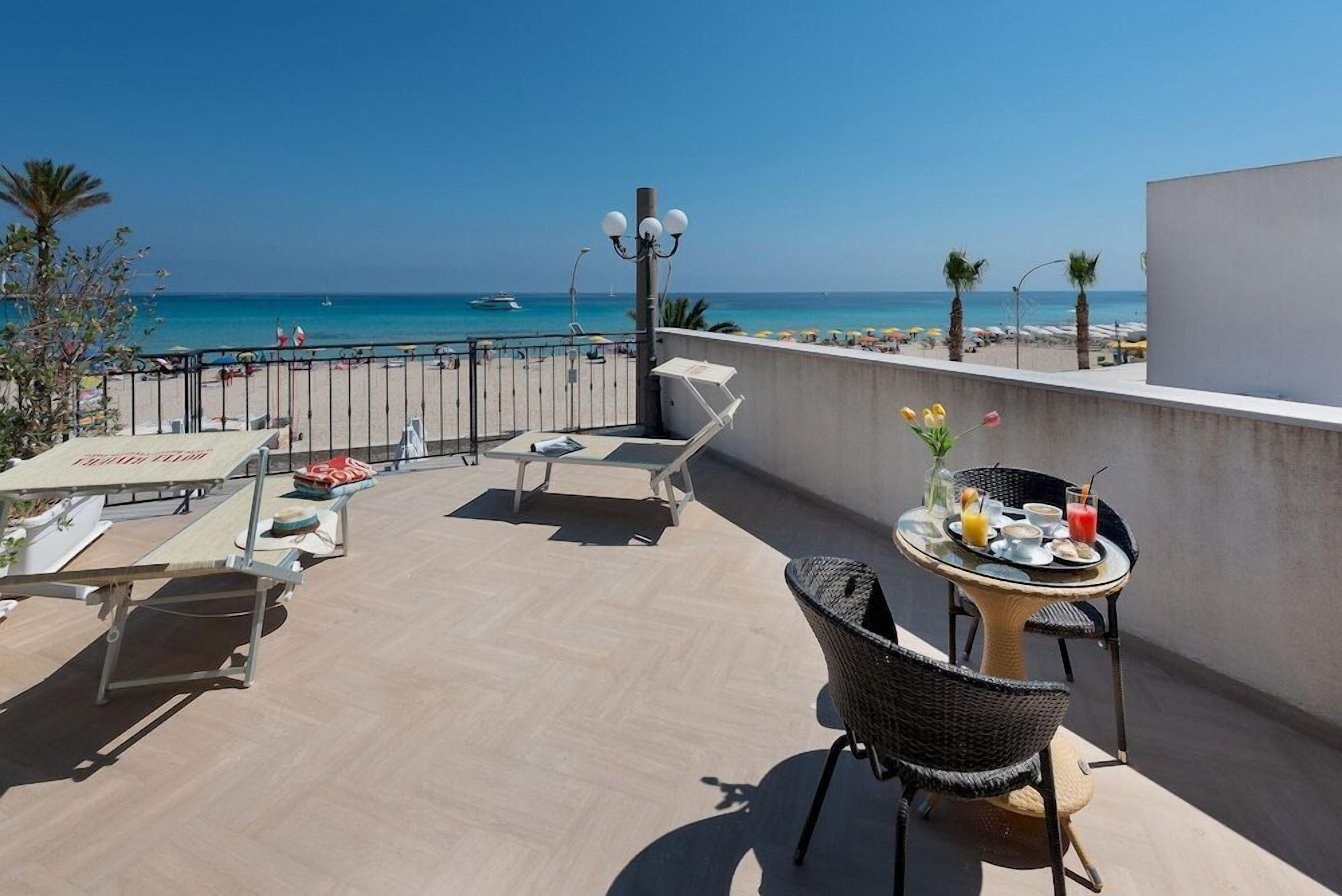 A rooftop terrace with a table set for dining, lounge chairs, and a view of the beach and sea.
