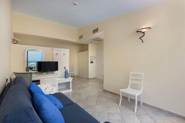 A modern hotel room with a sofa, TV, and a view of the sea.