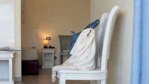 A white chair with a white towel draped over it, a blue towel hanging on a rack, and a white table with a lamp in the background. - Riviera (San Vito Lo Capo)