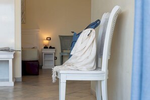 A white chair with a white towel draped over it, a blue towel hanging on a rack, and a white table with a lamp in the background.