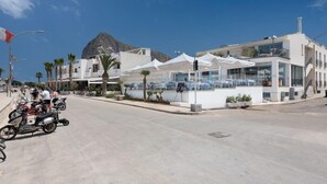 A modern building with a white facade, large windows, and a balcony overlooking a street with parked motorcycles. - Riviera (San Vito Lo Capo)