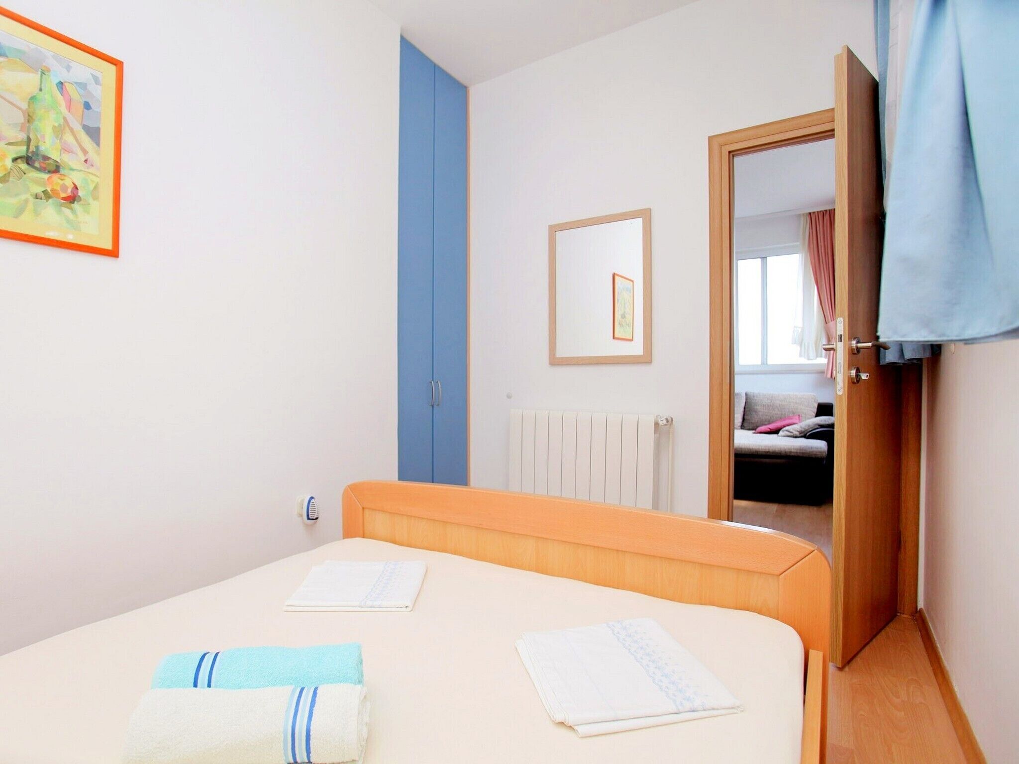 Un dormitorio con una cama, un radiador, una puerta que da a otra habitación y un cuadro enmarcado en la pared.