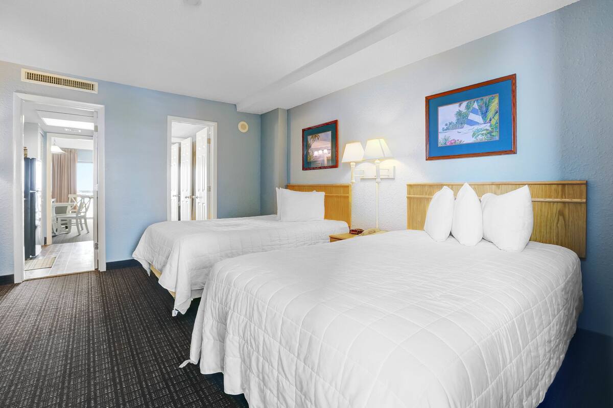 Habitación de hotel con dos camas, un baño a la vista a través de una puerta abierta y un cuadro en la pared.