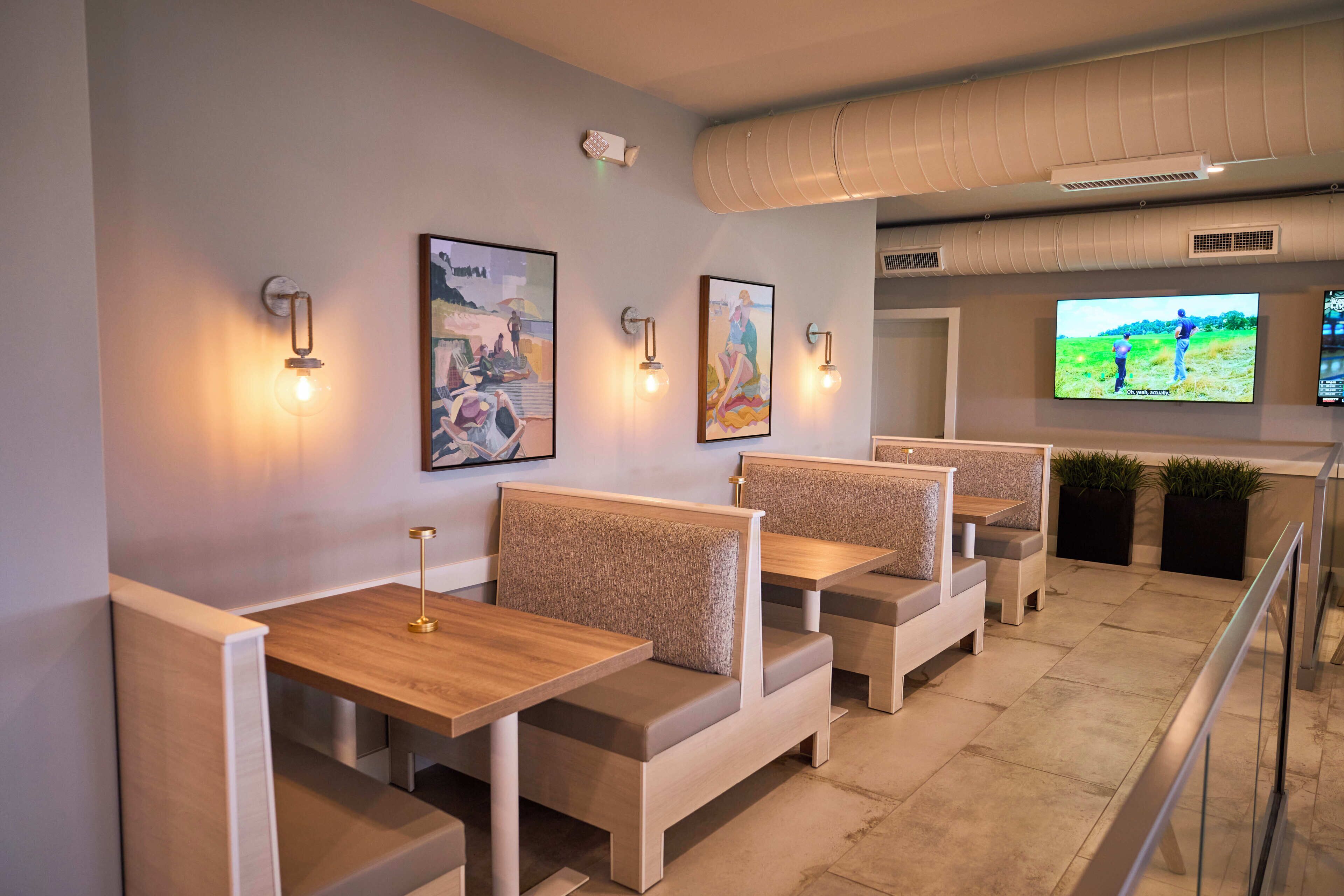 A modern restaurant with booth seating, wall-mounted artwork, and a television screen.