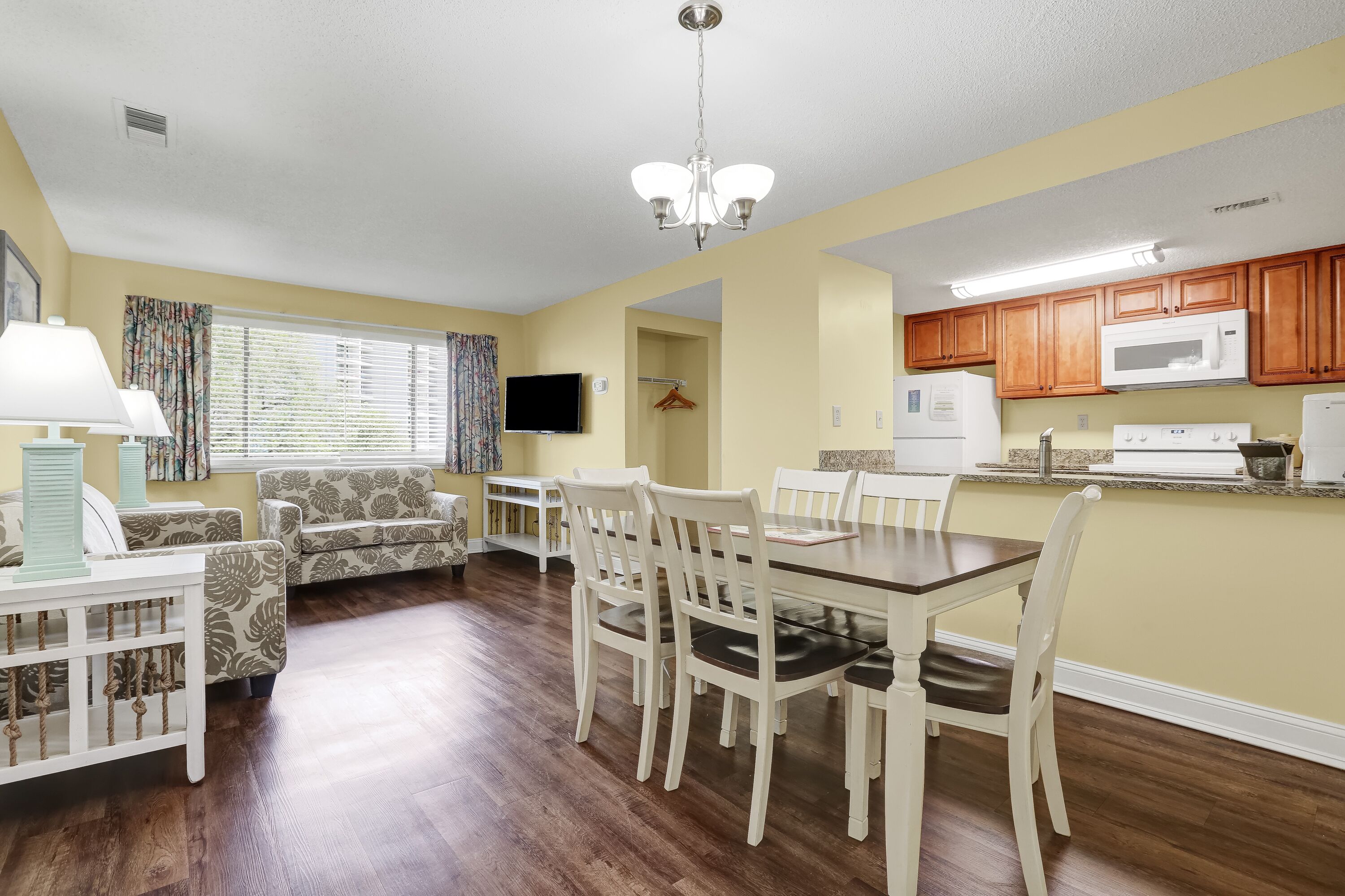 A compact living space with a dining area, kitchen, and a TV mounted on the wall.