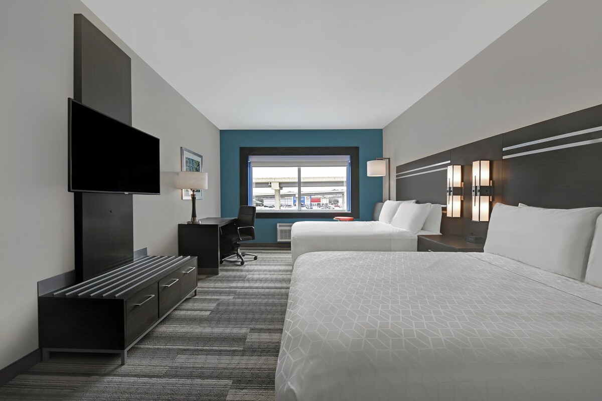 A hotel room with a bed, a desk, a TV, and a window with a view of the city.