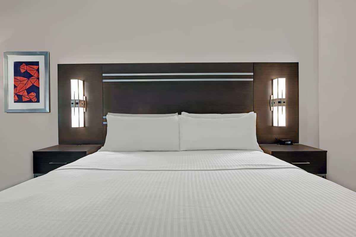 A modern hotel room with a large bed, two bedside tables, and wall-mounted lighting.