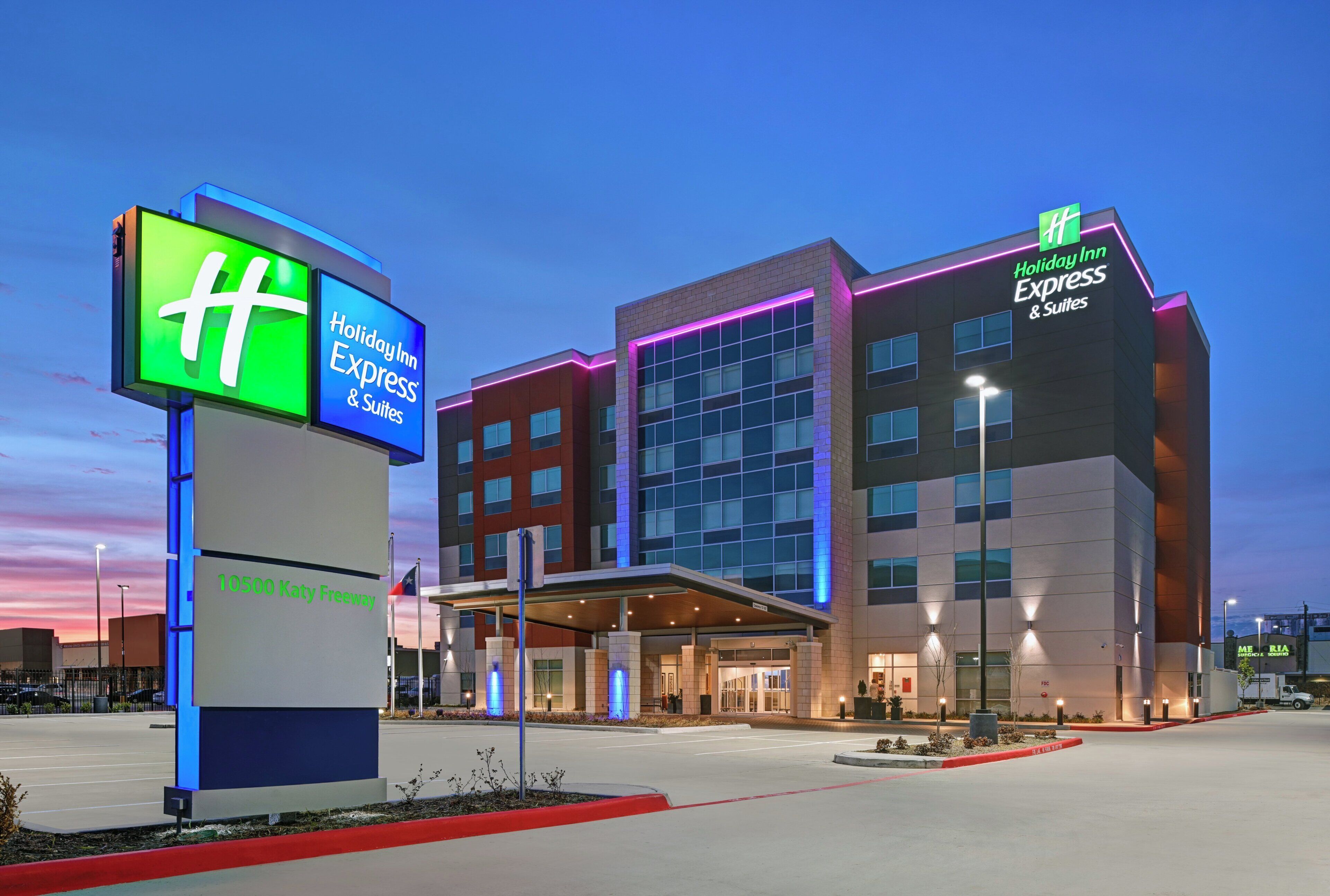 A Holiday Inn Express & Suites hotel with a prominent sign, a parking lot, and a clear sky.