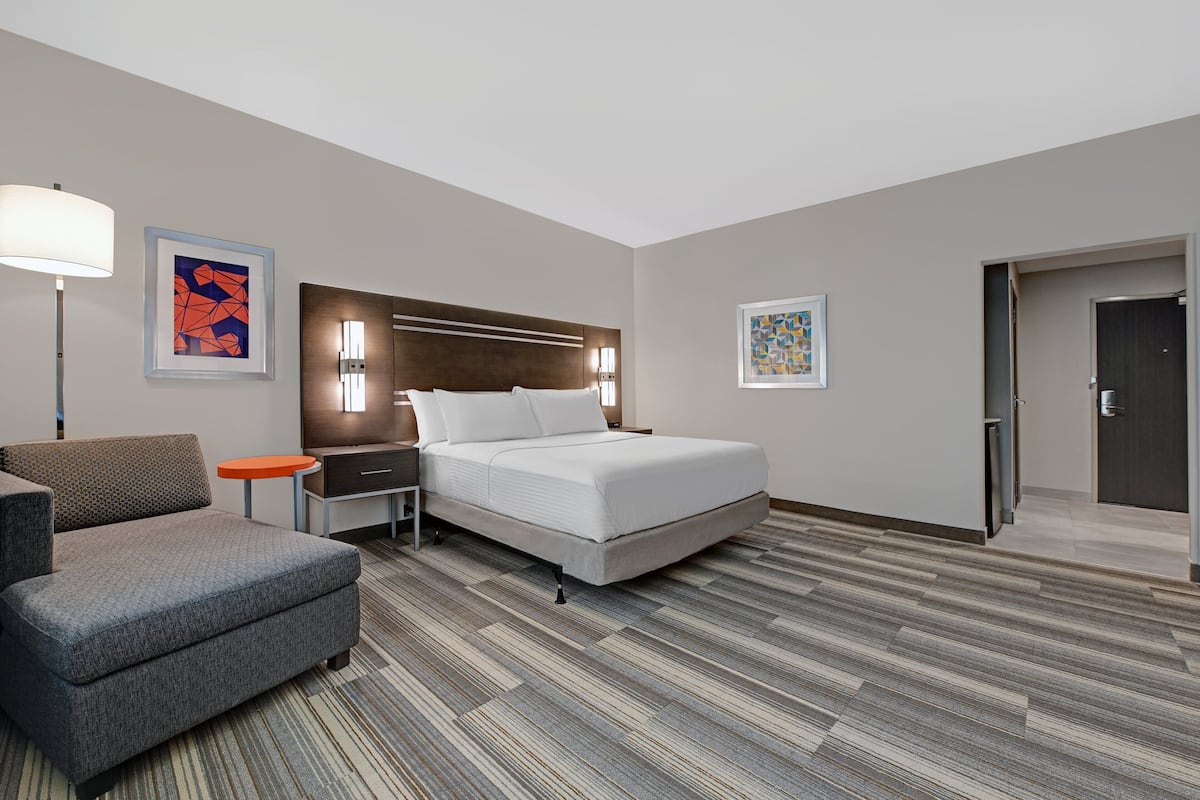 A hotel room with a bed, a nightstand, a lamp, a sofa, and artwork on the walls.