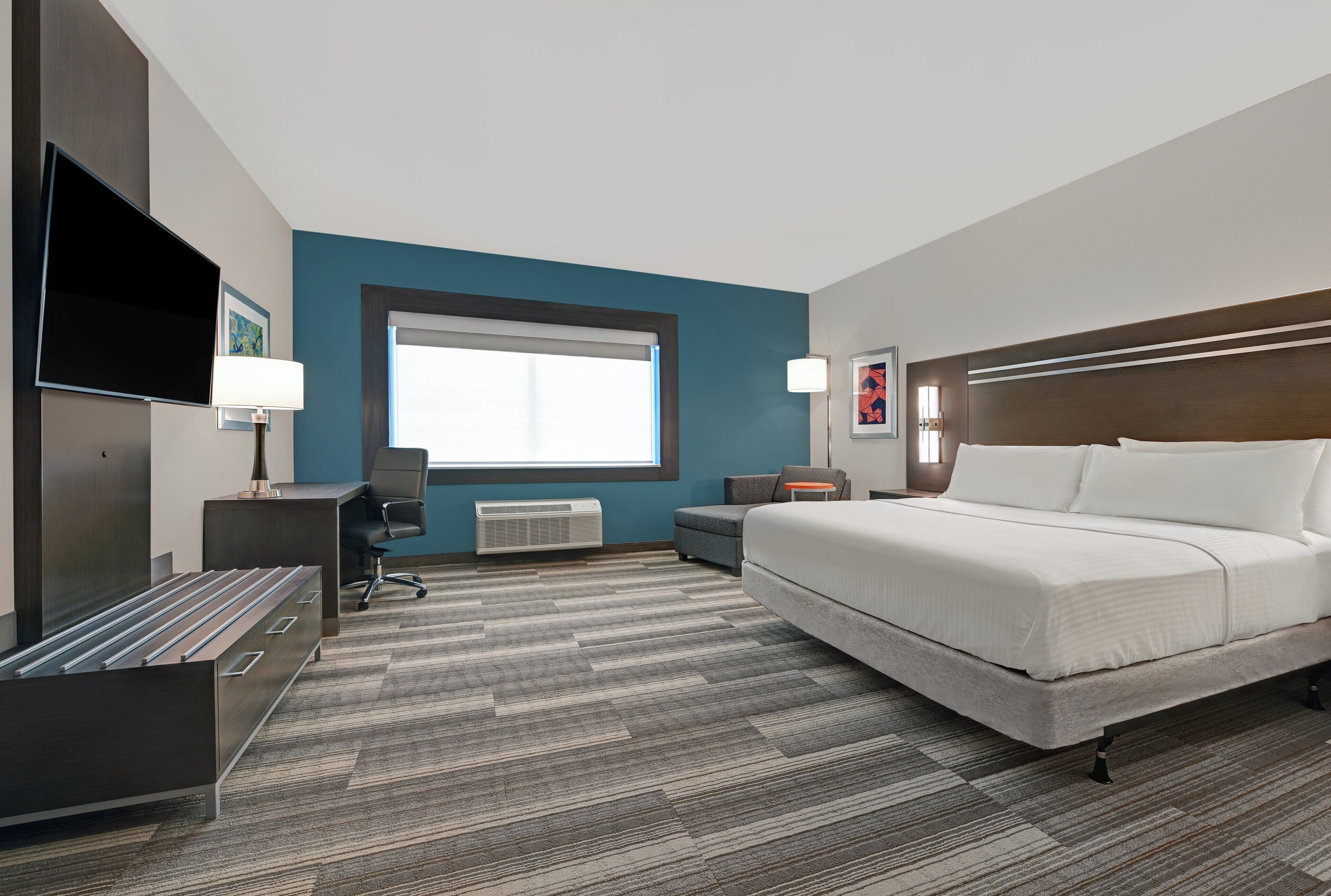 A hotel room with a bed, desk, chair, TV, and a window.
