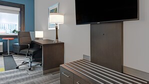 Een hotelkamer met een bureau, stoel, televisie, lamp en een groot raam.