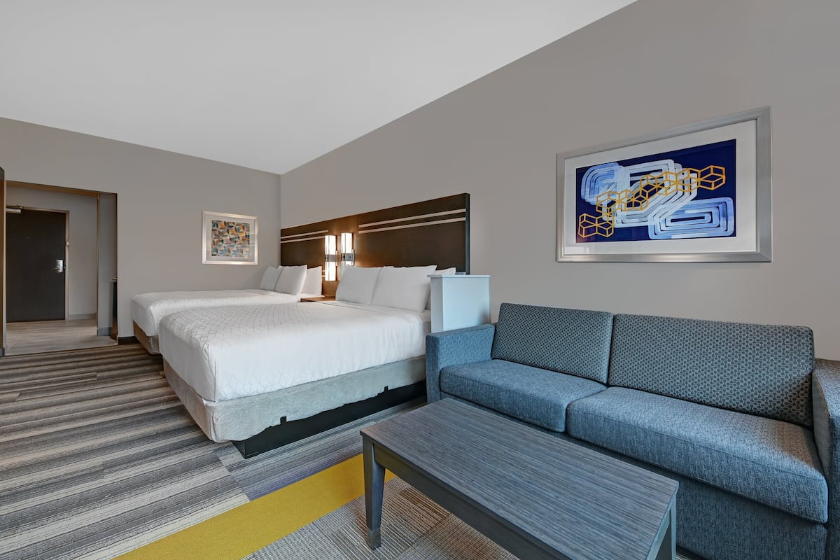 A hotel room with a large bed, a sofa, a coffee table, and a painting on the wall.