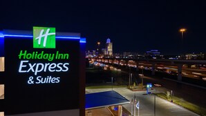 Een Holiday Inn Express & Suites bord met uitzicht op een stadshemel en een parkeerplaats 's nachts.
