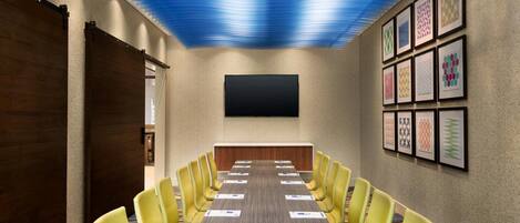 A conference room with a long table, yellow chairs, a flat-screen TV, and framed artwork on the walls.