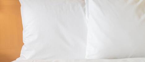 Cama con ropa blanca y almohadas frente a un cabecero de madera.
