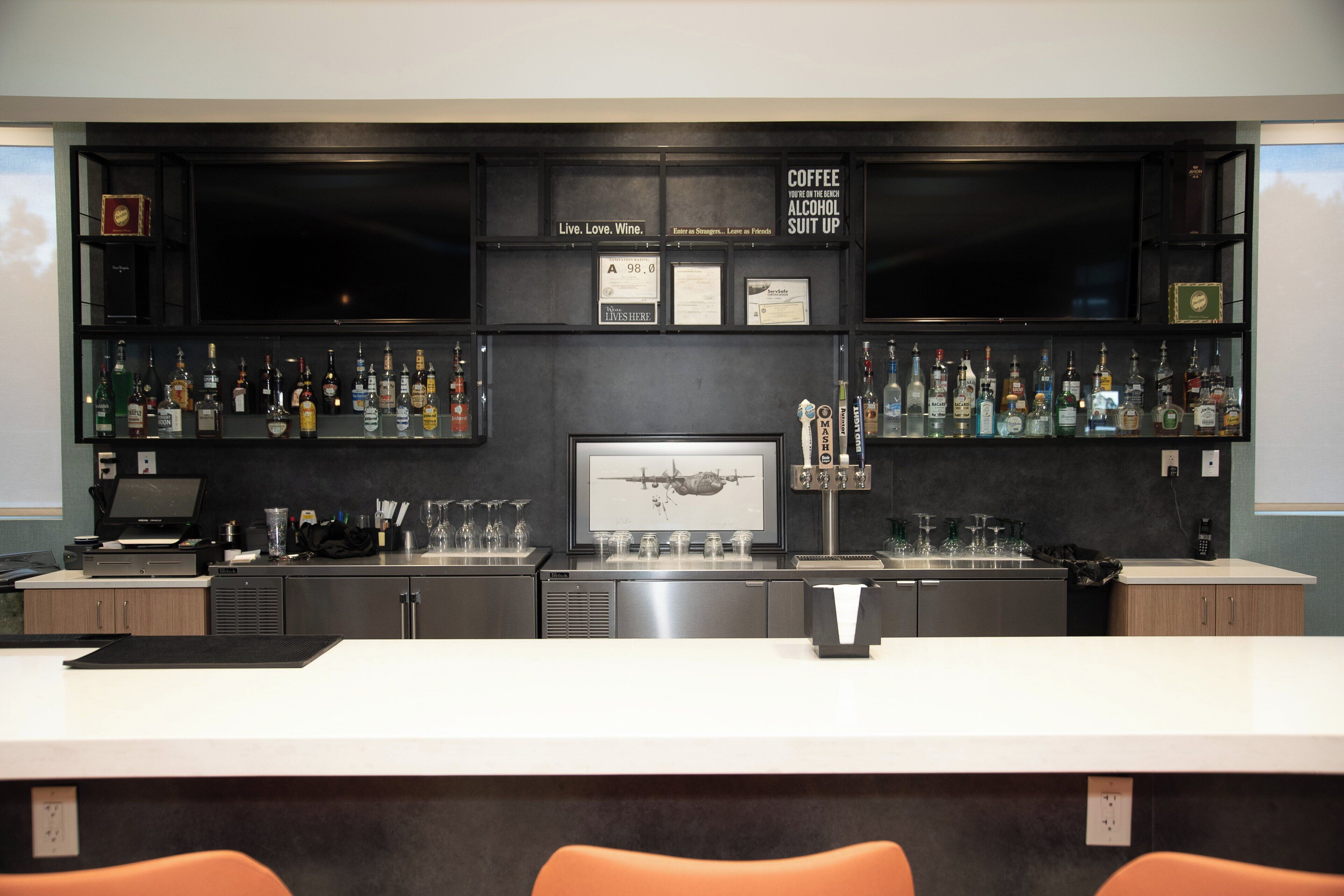 A bar area with a counter, shelves of liquor bottles, a framed picture, and a sign above the counter.