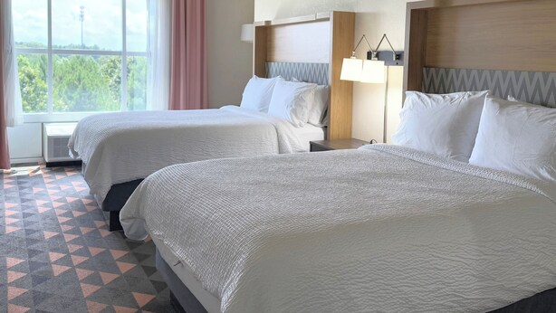 A hotel room with two beds, a large window with a view, a bedside table with a lamp, and a patterned floor. - Holiday Inn & Suites Fayetteville W-Fort Bragg Area by IHG (Fayetteville)