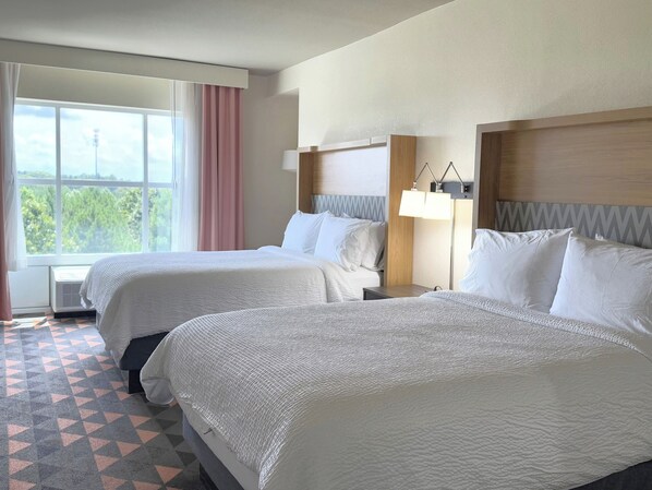 A hotel room with two beds, a large window with a view, a bedside table with a lamp, and a patterned floor. - Holiday Inn & Suites Fayetteville W-Fort Bragg Area by IHG (Fayetteville)