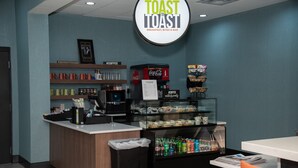 Een ontbijtbuffet met een Coca-Cola automaat, een glazen vitrine met snacks, en een bord met de tekst 'Toast to Toast Breakfast, Bites & Bar'.