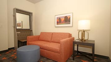 A hotel room with a sofa, ottoman, lamp, framed picture, and a mirror.