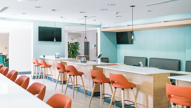 Een modern restaurant met een lange gedeelde tafel, aparte zitjes en oranje stoelen.