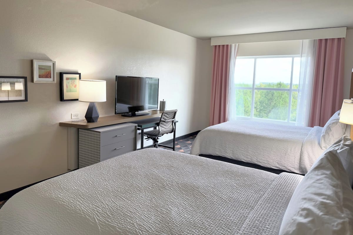 A hotel room with two beds, a desk with a computer, a television, and a window with curtains.