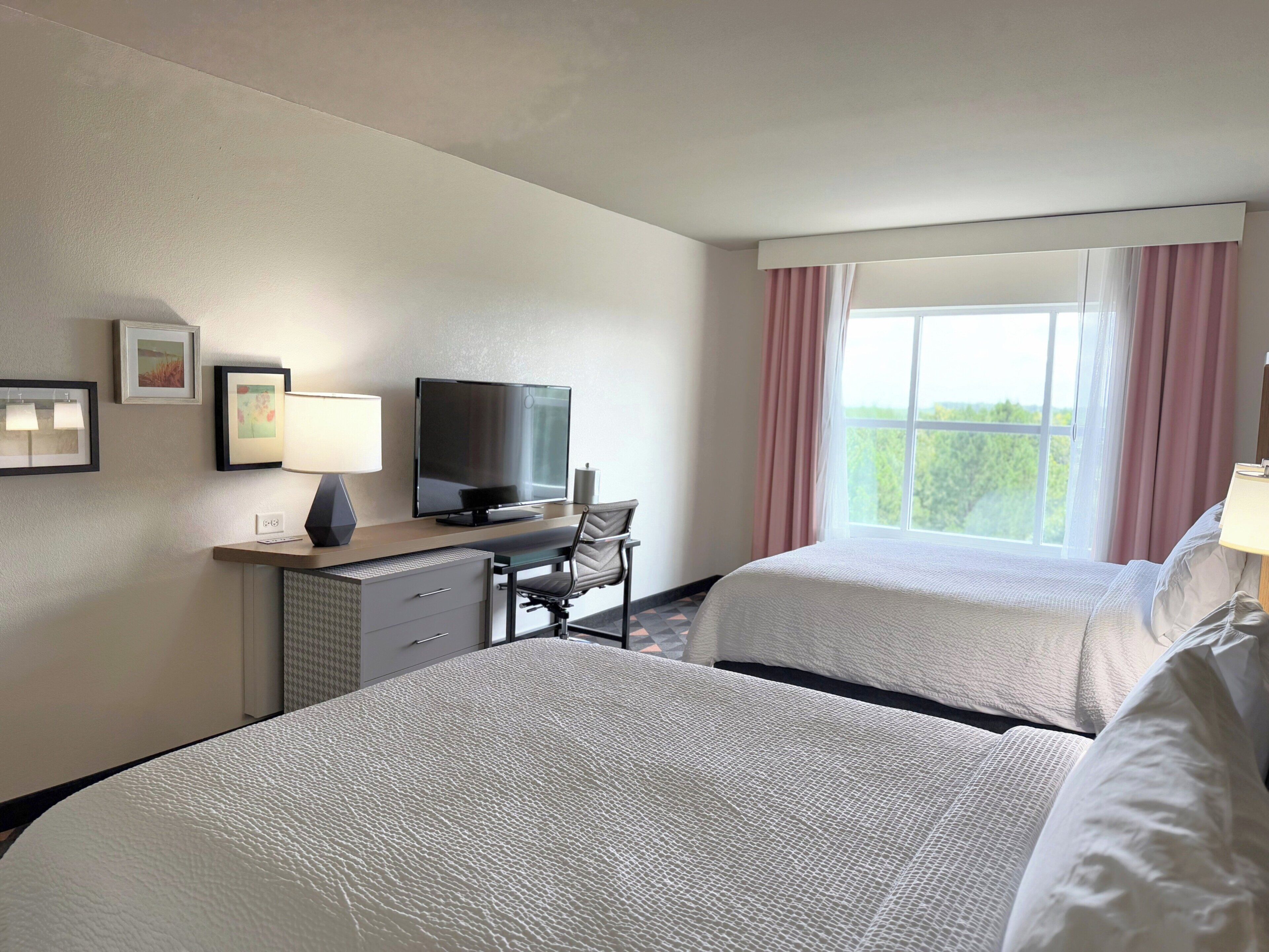 A hotel room with two beds, a desk with a computer, a television, and a window with curtains.