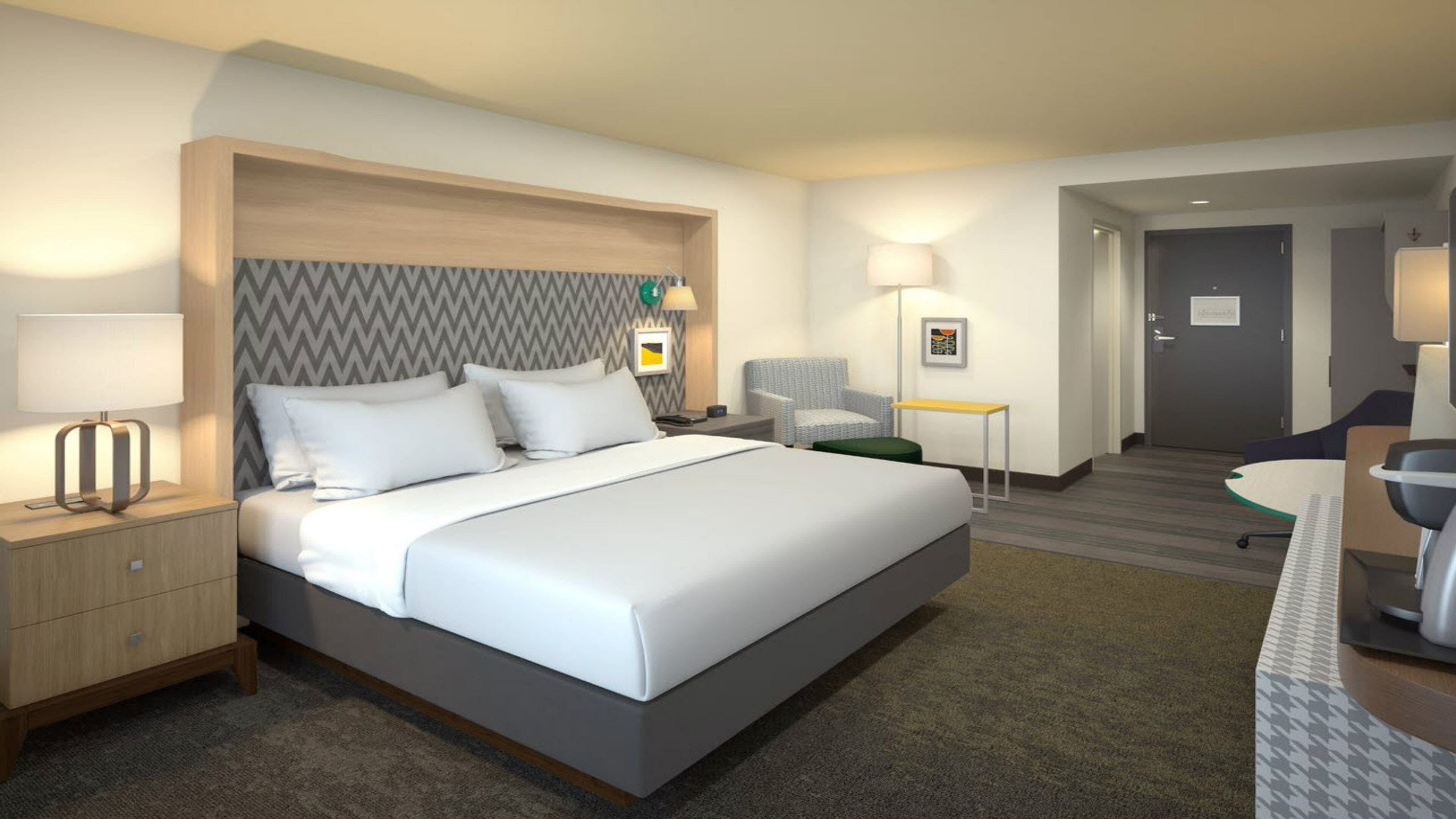 A hotel room with a bed, bedside table, lamp, chair, and a desk with a chair.