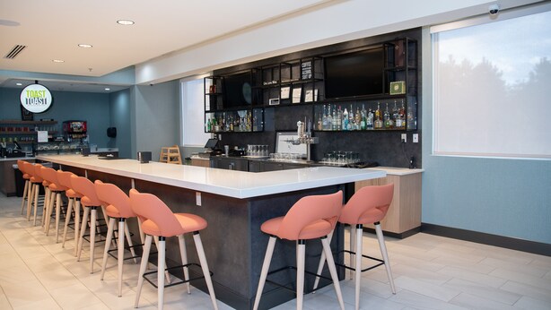 Un espace bar moderne doté d’un long comptoir, de nombreux tabourets et d’une grande variété de bouteilles d’alcool.