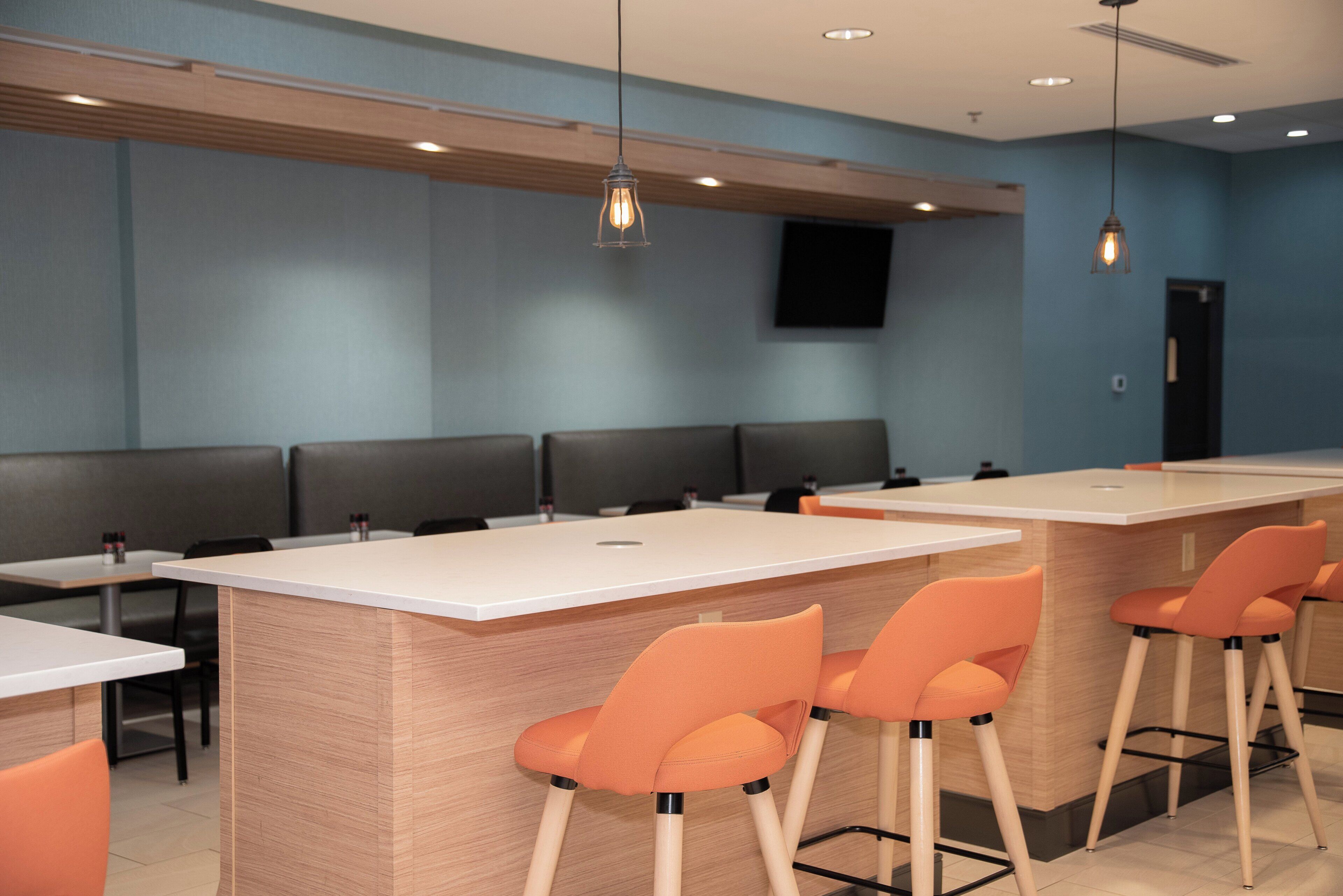 A modern restaurant interior with booths, high tables, and orange chairs.