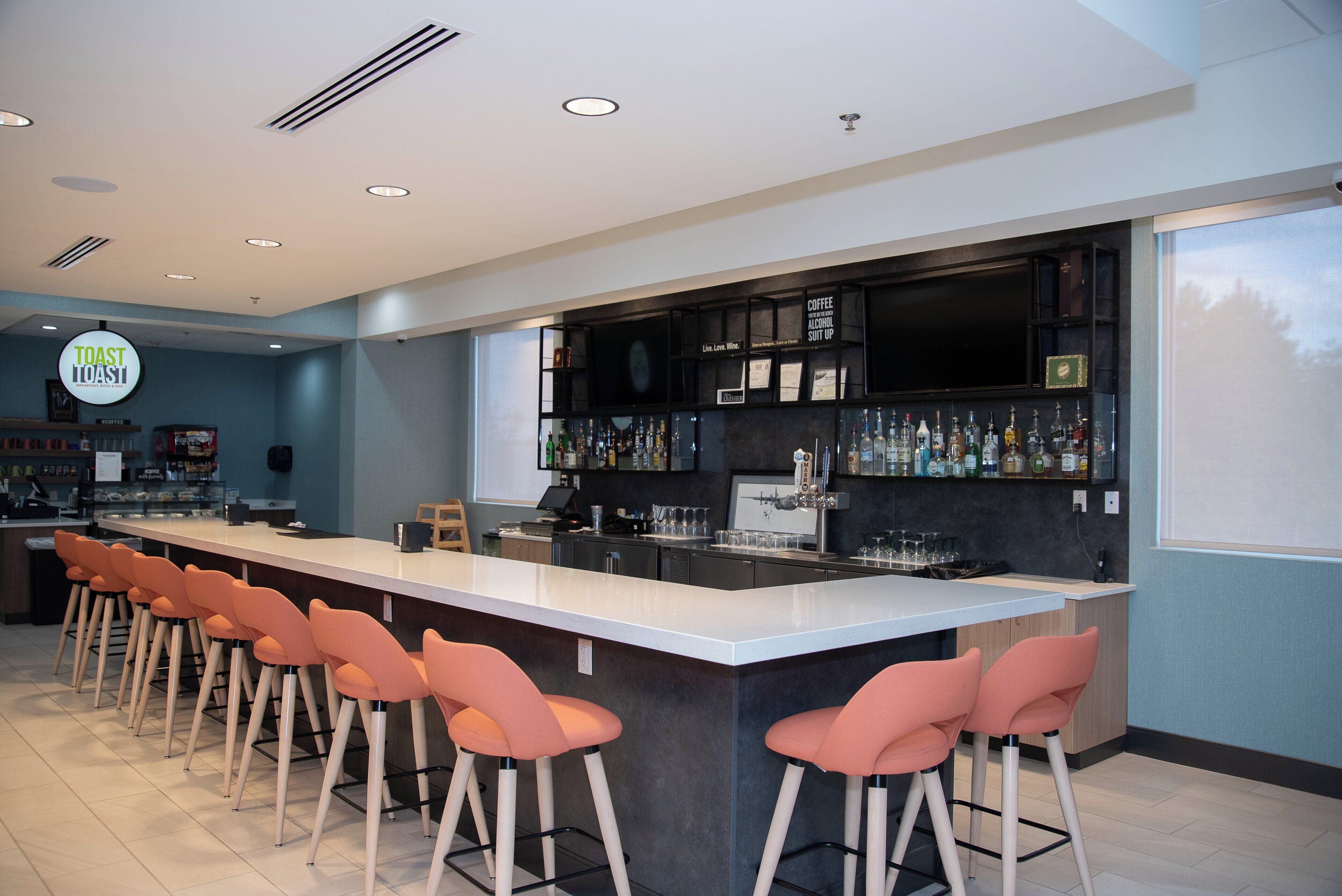 Zona de bar moderna con una barra larga, taburetes y una variedad de botellas de licor.