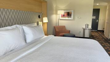 A hotel room with a large bed, a wooden headboard, a chair, a small table, and a lamp.