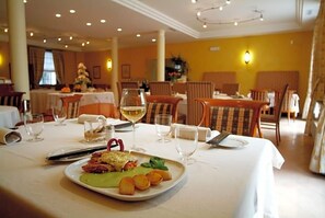 A dining area with tables set for a meal, featuring a plate of food and wine glasses.