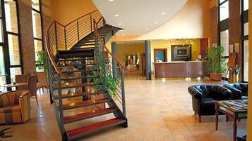 Eine geräumige Lobby mit einer zentralen Treppe, einer Sitzecke und einer Rezeption.