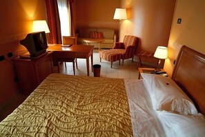 A hotel room with a bed, a desk, a chair, a television, and a lamp.