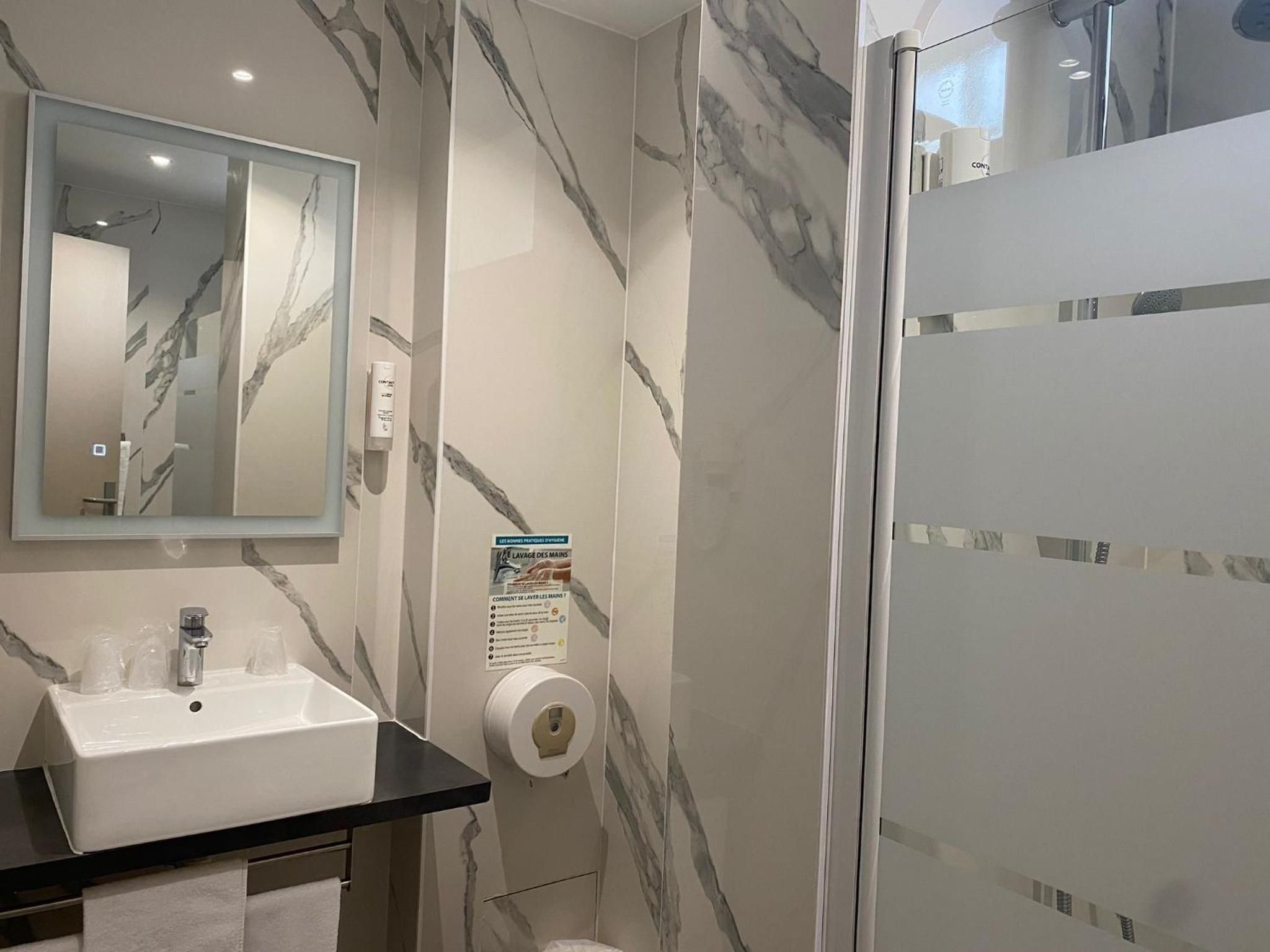 Une salle de bain moderne avec un mur en marbre, un lavabo, un miroir et un espace douche.