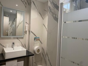 Un baño moderno con pared de mármol, lavamanos, espejo y zona de ducha.