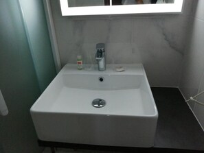 A bathroom with a white sink, a mirror, and a small bottle of hand soap. - Contact Hôtel Foch (Besancon)
