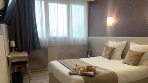Una camera d'albergo con un letto, una scrivania, una sedia, un termosifone e una finestra con tende.
