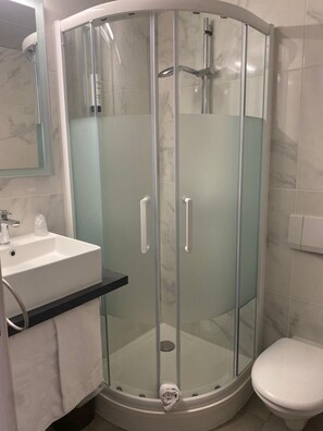 A bathroom with a glass-enclosed shower, a sink, and a toilet. - Contact Hôtel Foch (Besancon)