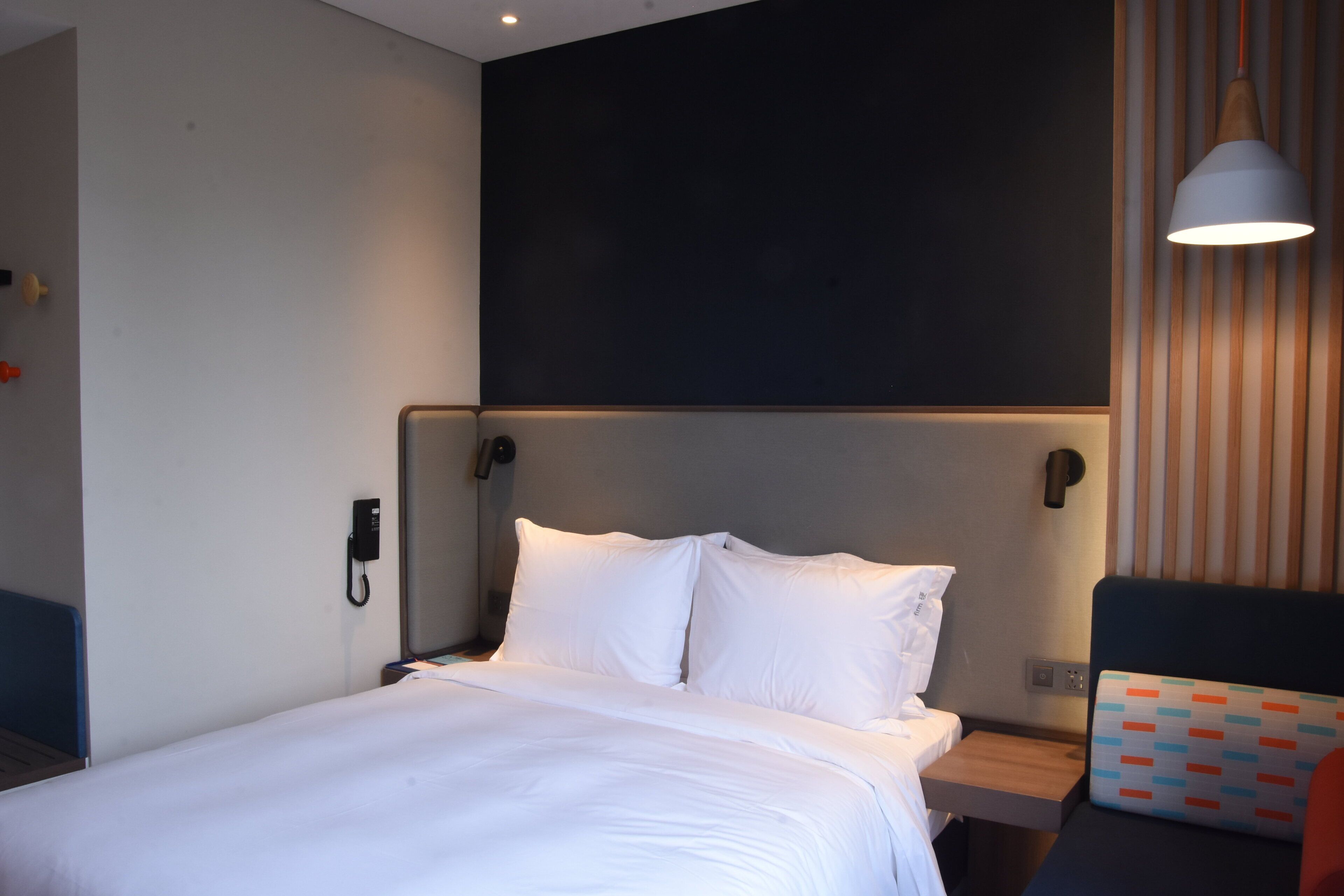Quarto de hotel com cama, mesas de cabeceira, telefone e luminária.