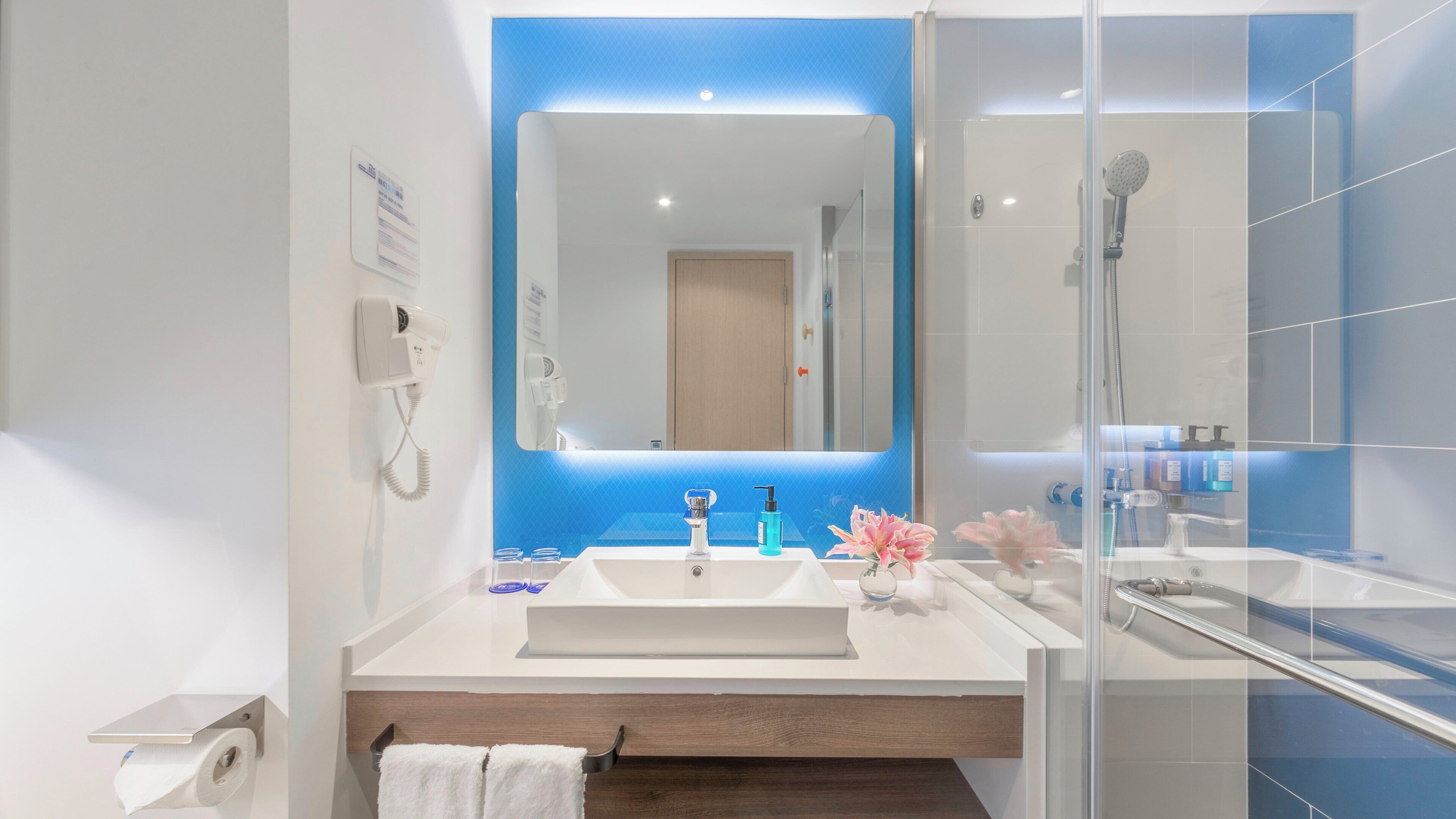 A modern bathroom with a large mirror, a sink, a shower, and a towel rack.