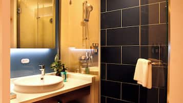 A bathroom with a sink, mirror, shower, and black tiled walls.