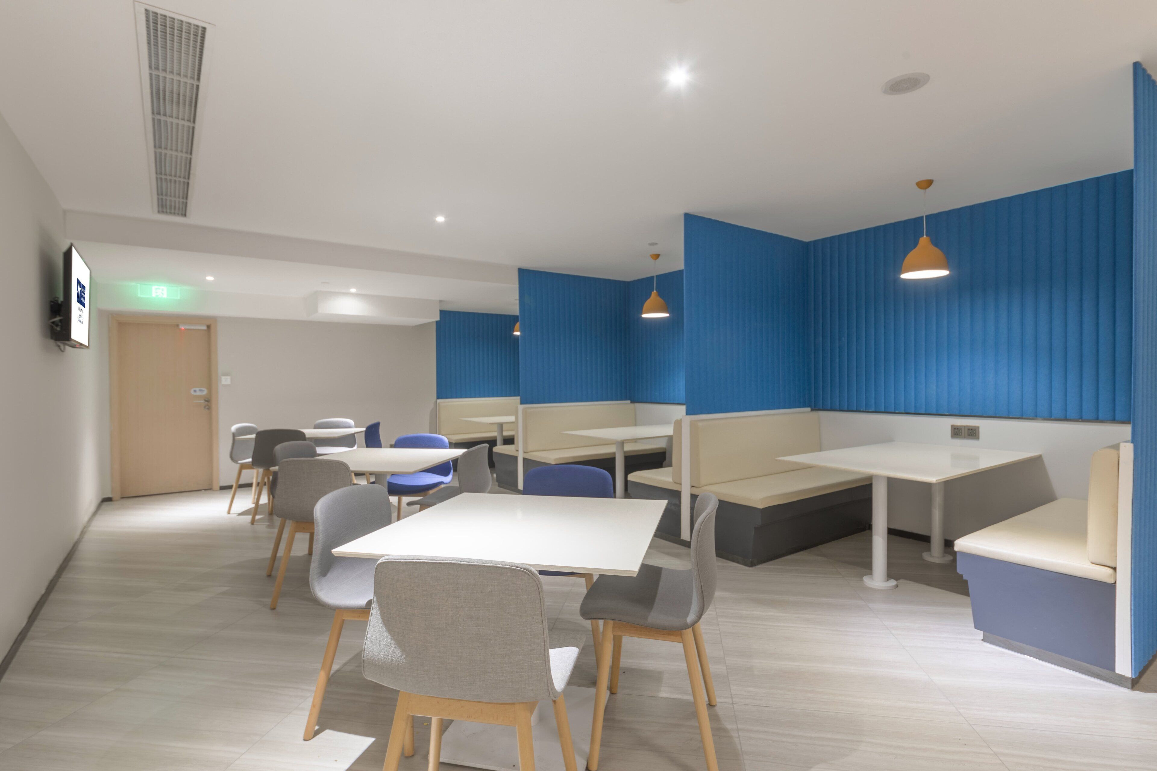 Zona pranzo moderna con tavoli bianchi e sedie grigie, pareti di accento blu e illuminazione a sospensione.