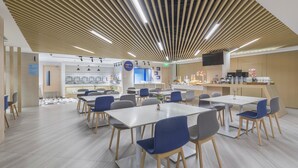 A modern cafeteria with multiple tables and chairs, a kitchen area, and a flat-screen TV mounted on the wall. - Holiday Inn Express Shanghai Gubei by IHG (Shanghai)