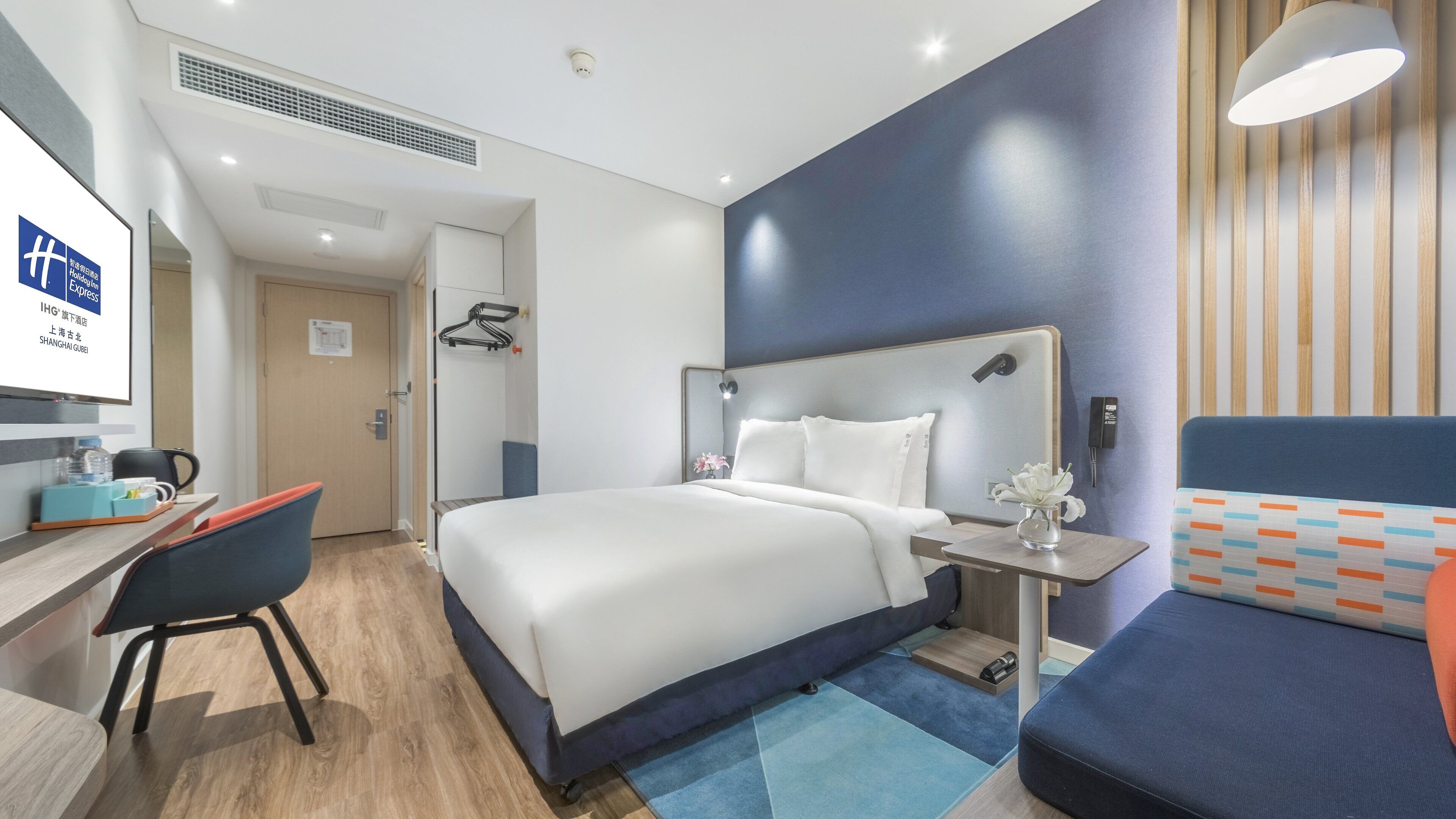 Une chambre d’hôtel comprenant un lit, une table de chevet, une chaise, un bureau et une petite table sur laquelle est posé un vase.