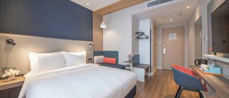 A modern hotel room with a large bed, a desk with a chair, a mirror, and a small table with a vase of flowers.