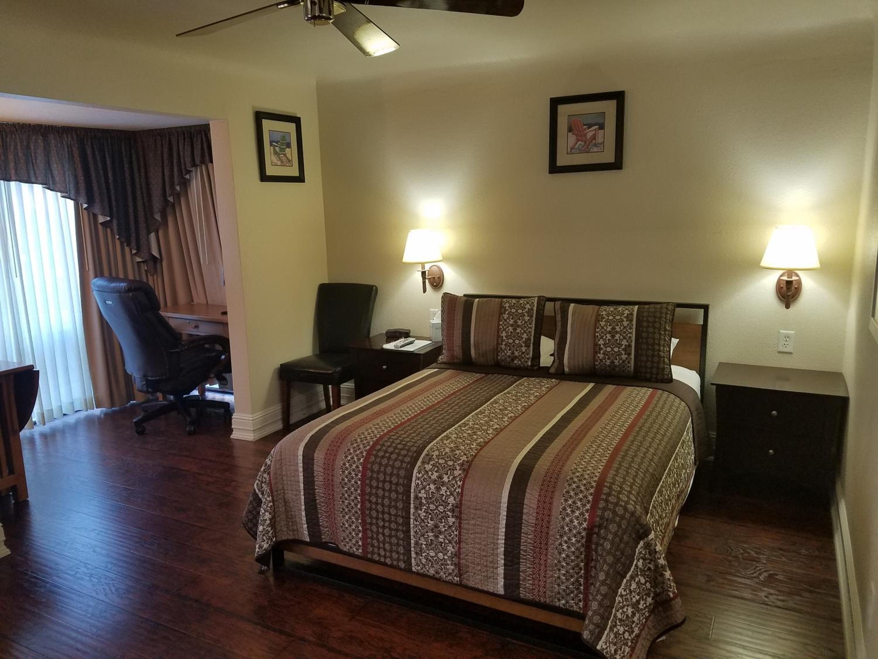 Una habitación de hotel con una cama grande, dos lámparas de noche, un escritorio con una silla y un ventilador de techo.