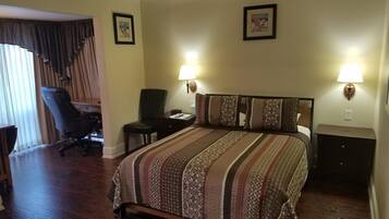 Una habitación de hotel con una cama grande, dos lámparas de noche, un escritorio con una silla y un ventilador de techo.