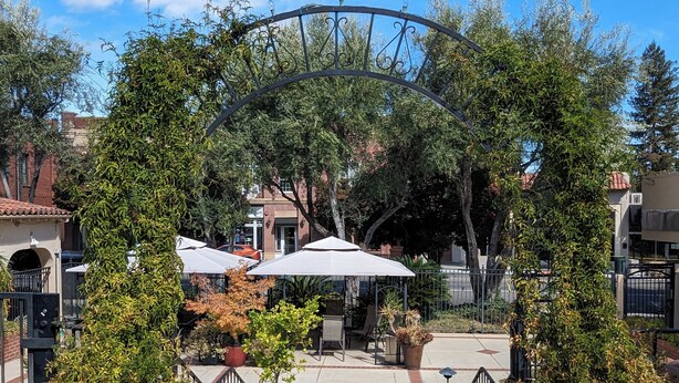 An outdoor patio area with a metal archway, potted plants, and outdoor seating. - Los Gatos Garden Inn Hotel (Los Gatos)